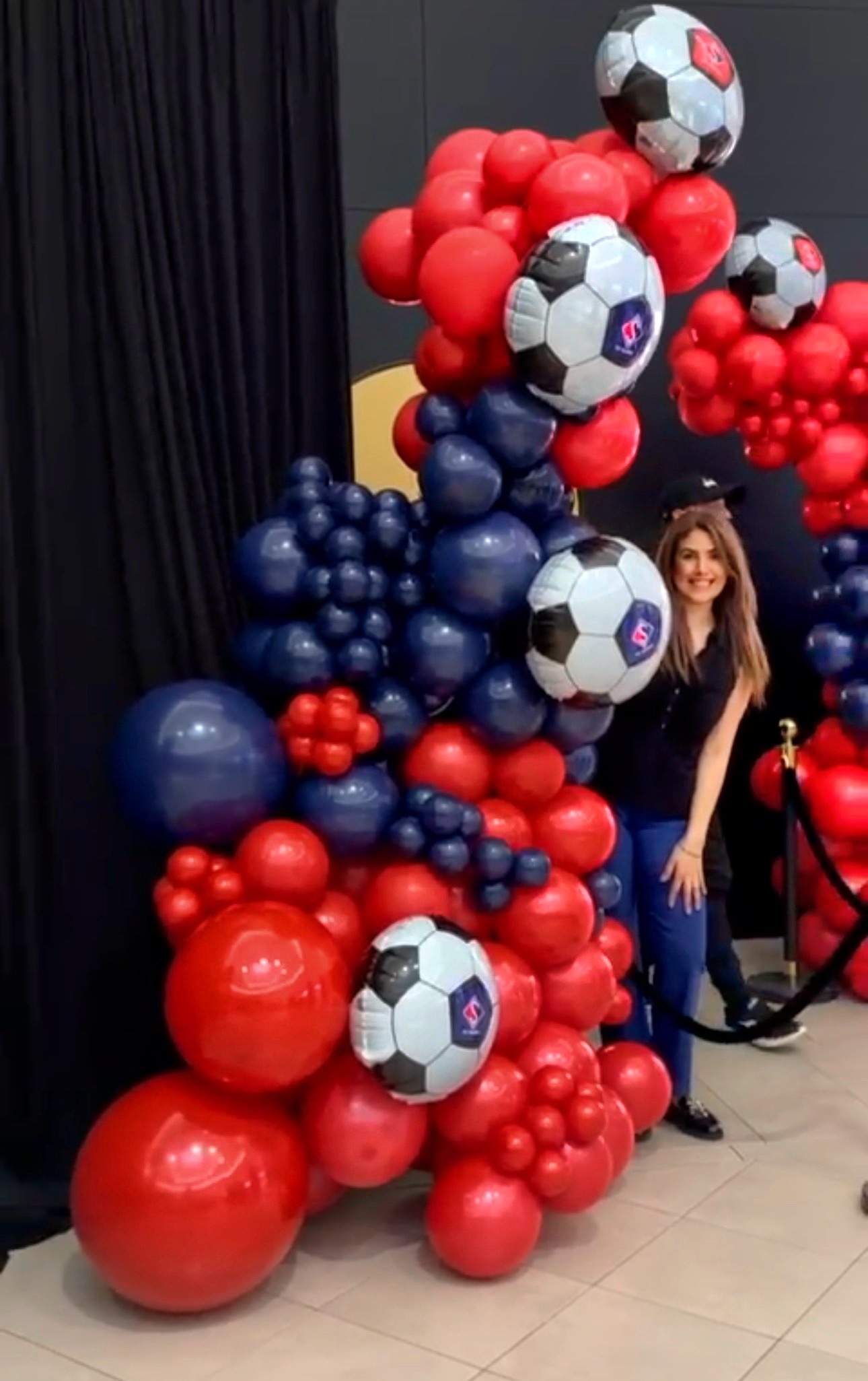 Colonnes de ballons rouges et bleu marine avec ballons mylar en forme de ballon de football, et une femme souriante