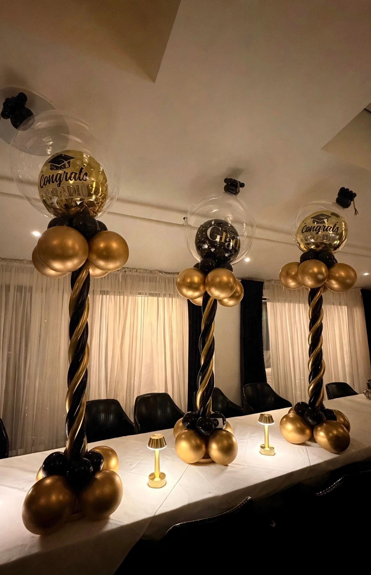Trois colonnes torsadées de ballons dorés et noirs surmontées de ballons « Congrats Grad », décor de salle de réception