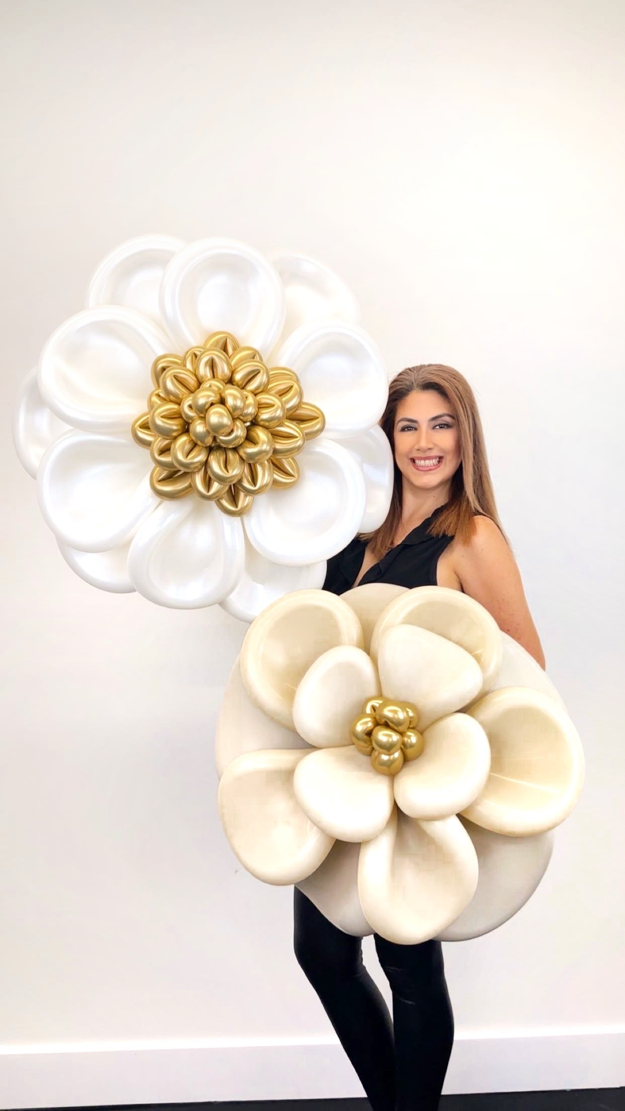 Deux grandes fleurs sculpturales en ballons blancs et dorés présentées par une artisane